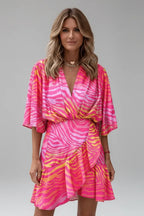 Model wearing a pink zebra-print mini wrap dress with flutter sleeves and layered gold necklaces