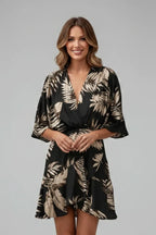 Model wearing a black and gold palm leaf print wrap mini dress with batwing sleeves