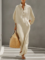Woman in oatmeal linen maxi dress with mandarin collar and button placket, holding a woven straw tote, front view