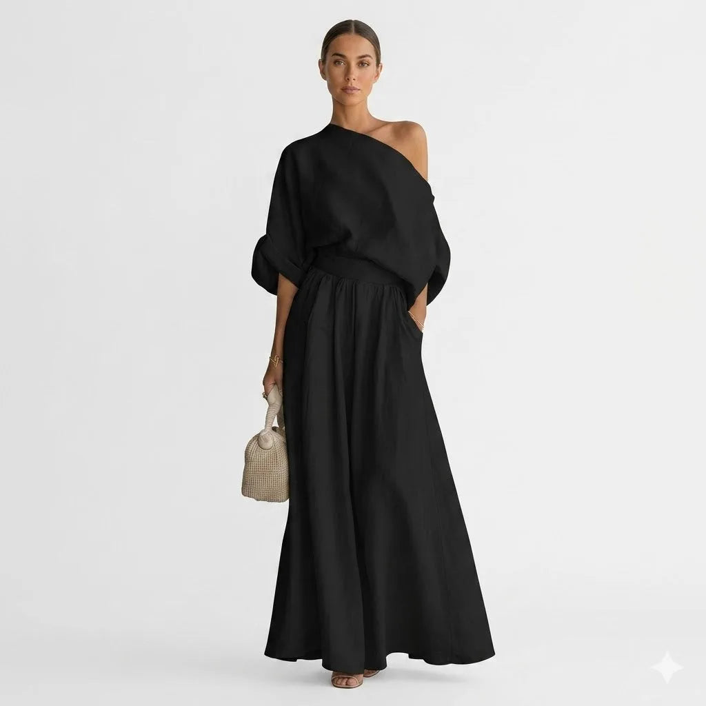 Woman in black one-shoulder linen-look maxi set with billowy sleeves, cuffed cuffs and flowing wide-leg skirt against a plain studio backdrop