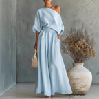 Sky blue one-shoulder maxi set with batwing sleeve and gathered waist skirt, styled with heeled sandals and a woven handbag