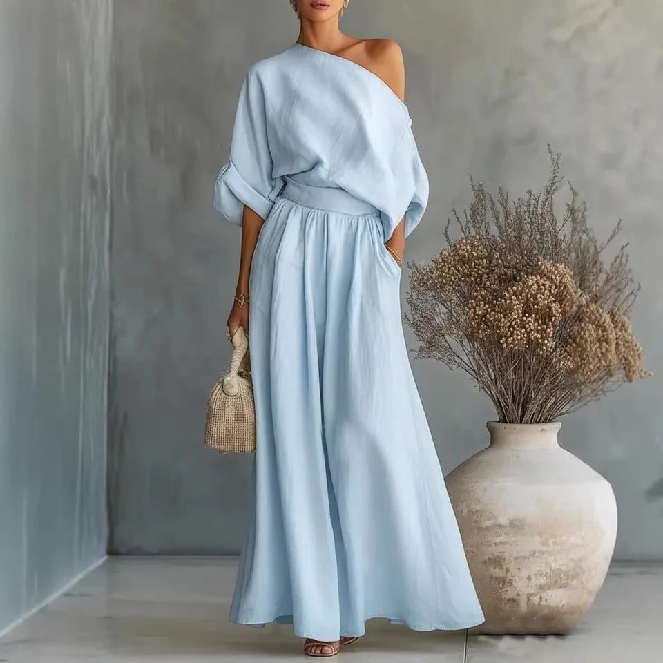 Sky blue one-shoulder maxi set with batwing sleeve and gathered waist skirt, styled with heeled sandals and a woven handbag