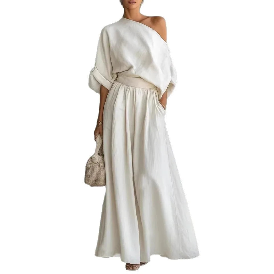 White one-shoulder top and maxi skirt set shown on plain background, highlighting the draped neckline and gathered waistband