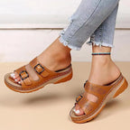 Side view of tan brown buckle sandal with perforated floral cutouts, worn on foot with cropped jeans and beaded anklet
