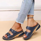 Navy blue leather sandal with two adjustable buckles and cushioned footbed, side profile on model against light wall