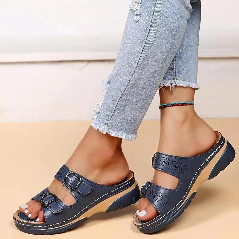 Navy blue leather sandal with two adjustable buckles and cushioned footbed, side profile on model against light wall