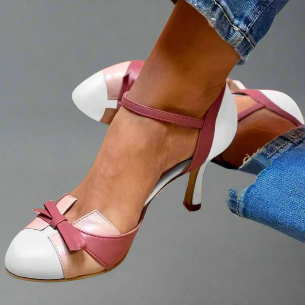 Pair of pink and white colourblock heels with bow trim shown from above, worn with cuffed denim jeans.