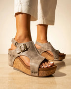 Front angle of beige distressed faux leather wedge sandal with brass buckle, cutout sides and studded cork wedge heel