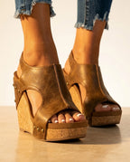 Close-up front view of brown faux leather wedge sandals with open toe, cutout detail and stacked cork platform sole, worn with denim jeans