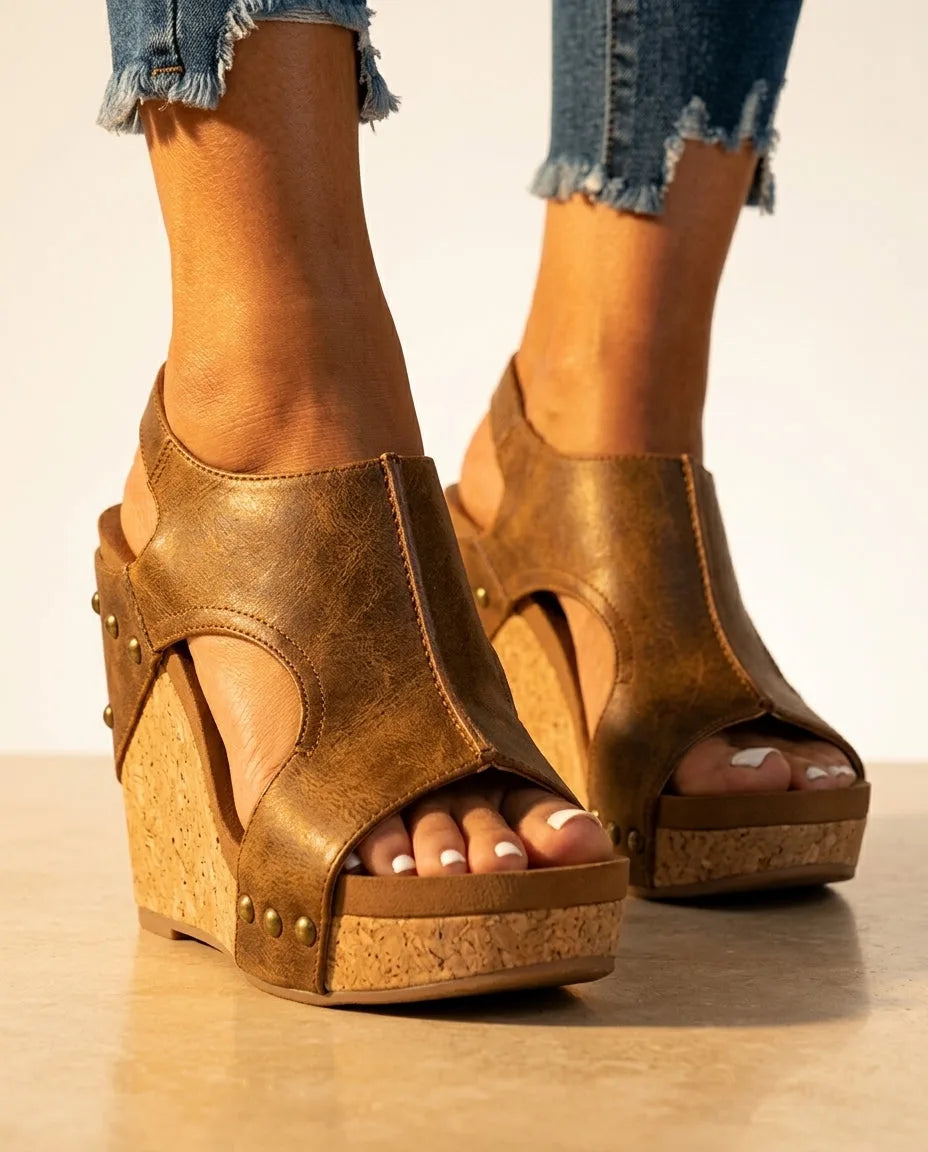 Close-up front view of brown faux leather wedge sandals with open toe, cutout detail and stacked cork platform sole, worn with denim jeans