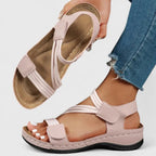 Pink strappy sandal held in hand showing cushioned tan footbed and crisscross ankle strap design