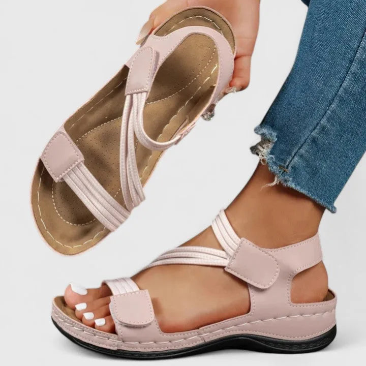 Pink strappy sandal held in hand showing cushioned tan footbed and crisscross ankle strap design