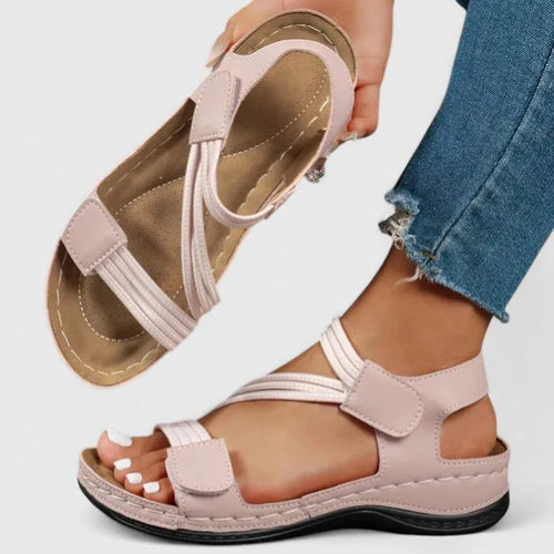 Pink strappy sandal held in hand showing cushioned tan footbed and crisscross ankle strap design
