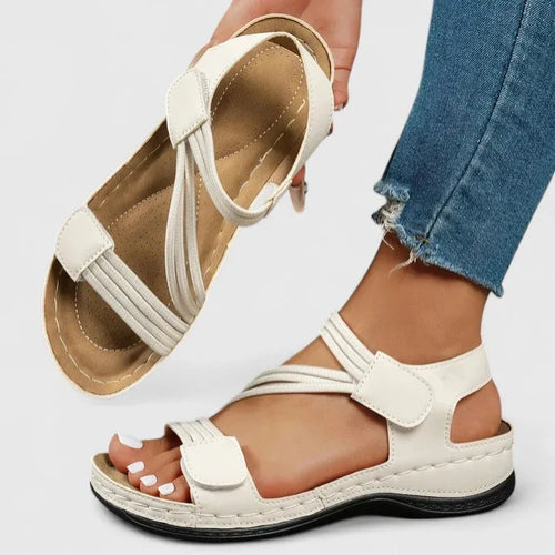 White strappy sandal held up revealing contoured padded insole with stitched arch support detail