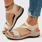 Khaki strappy sandal worn on foot showing crisscross front straps and stitched wedge sole