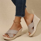 Side view of khaki suede crisscross wedge sandal with woven espadrille-style platform sole and gold heart anklet