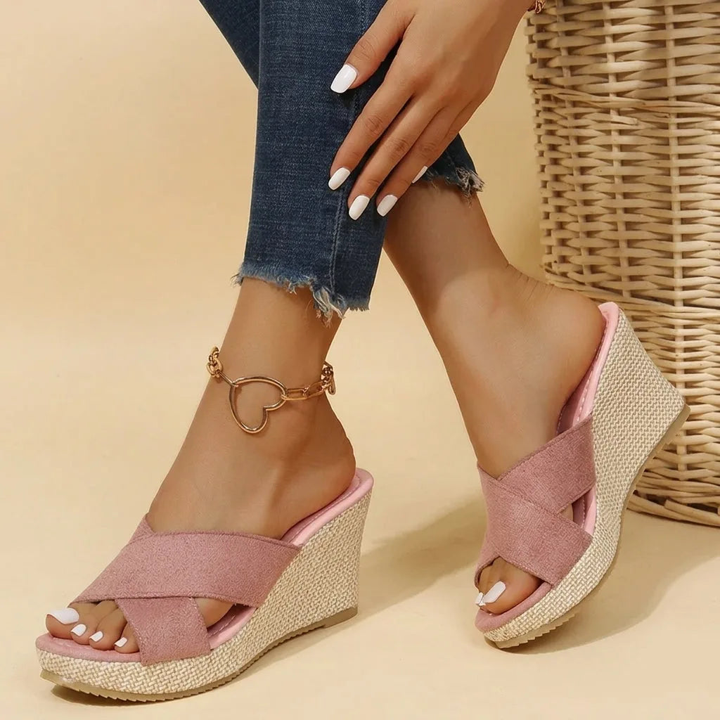 Model wearing pink suede crisscross wedge sandals paired with cropped denim jeans beside a woven basket