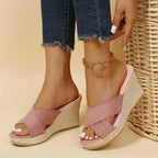 Front angle of pink suede crisscross wedge sandals resting against a woven wicker basket