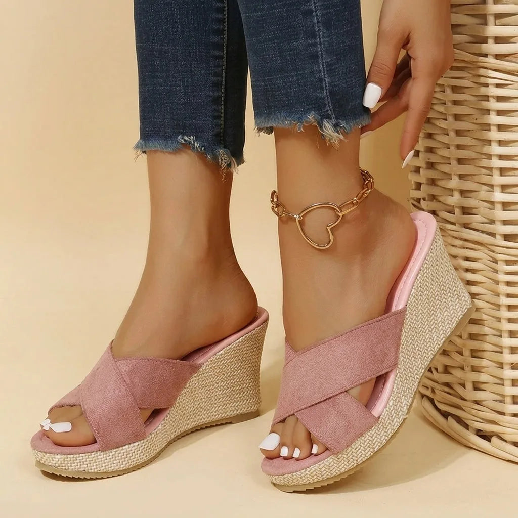Front angle of pink suede crisscross wedge sandals resting against a woven wicker basket