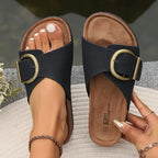 Close view of black crossover sandals with brass buckles on feet, cork-look footbed and cushioned tan insole visible