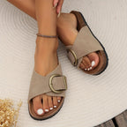 Top-down view of blush pink sandals held by hand, showing the soft suede-look footbed and brass buckle closure