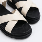 Close-up of cream white crossover toe straps showing stitched faux leather texture against the black footbed
