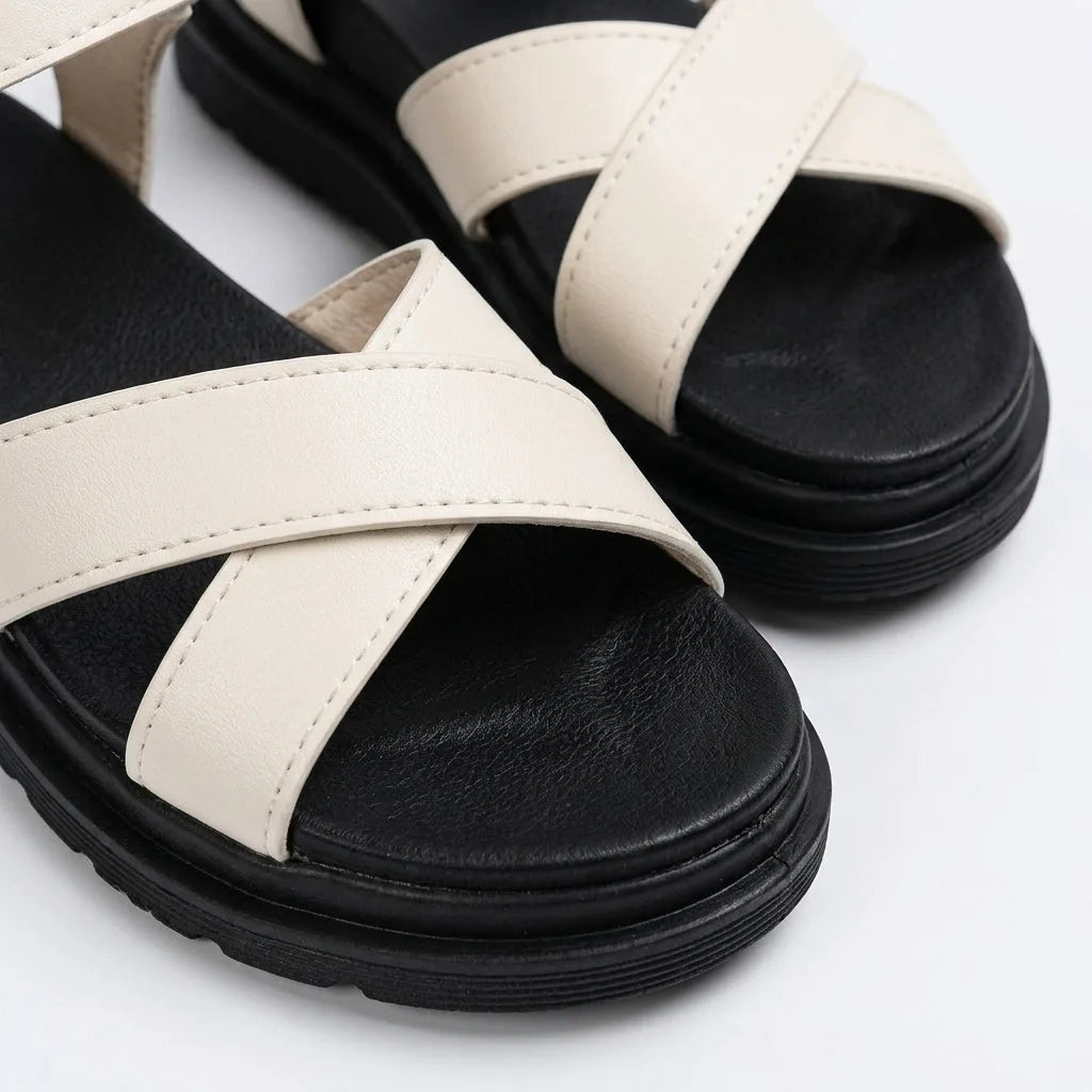 Close-up of cream white crossover toe straps showing stitched faux leather texture against the black footbed