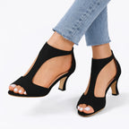 Front angle of black suede peep-toe heels highlighting the T-strap silhouette and curved heel shape