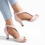 Pink suede T-strap sandals lifted mid-step, showing the open toe and slim kitten heel profile