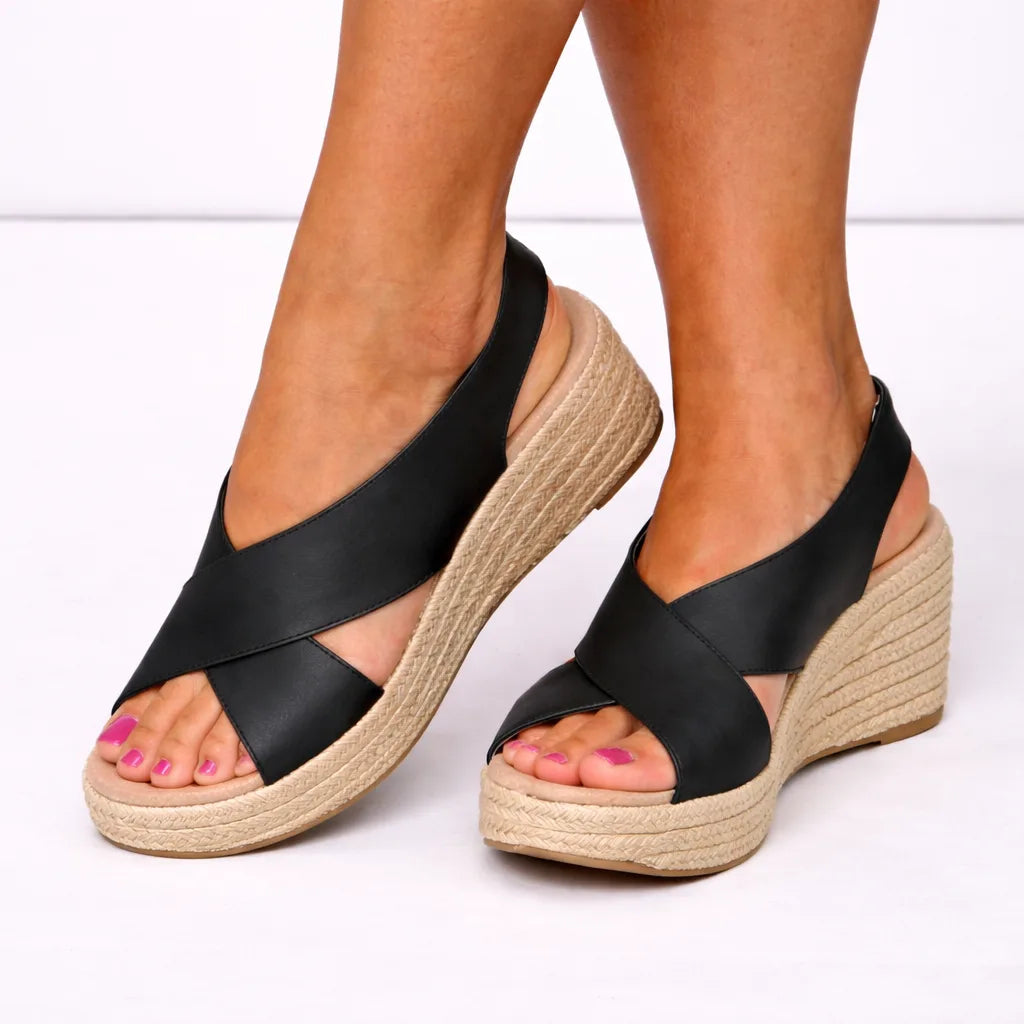 Close view of black crossover strap espadrille wedge sandals with woven jute platform sole, worn on feet.