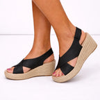 Black espadrille wedge sandal with ankle buckle strap, viewed from the side showing the woven heel height.