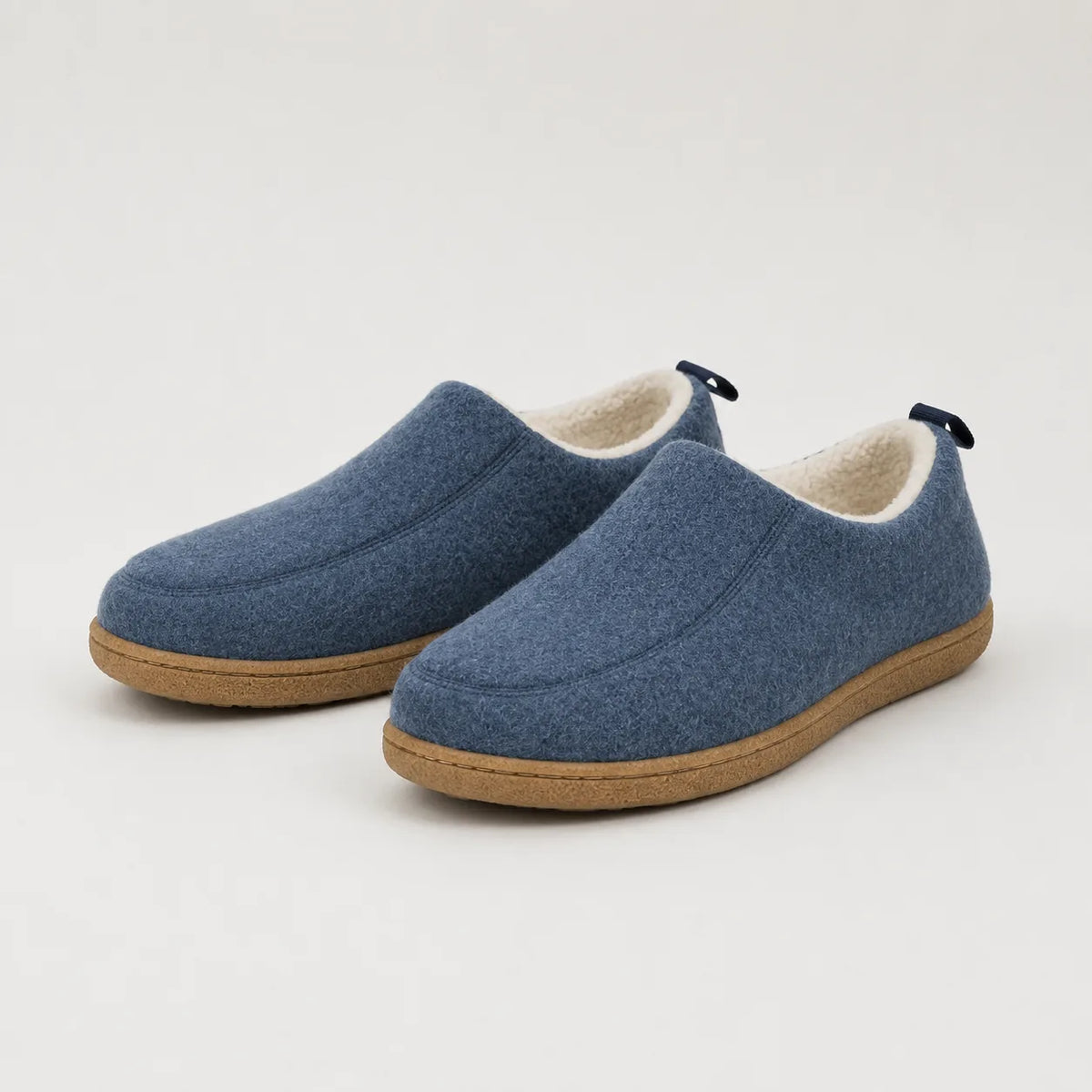 Side view of a pair of slate blue wool felt slip-on slippers with cream fleece lining and tan rubber sole