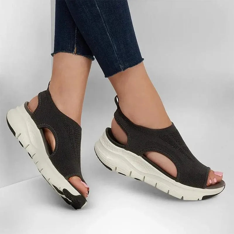 Woman wearing charcoal grey knit sandals with jeans, showing open heel and chunky white sole from the side