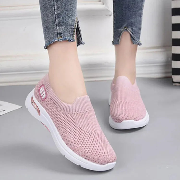 Model wearing pink knit slip-on sneakers with cropped jeans, close-up side view on grey floor