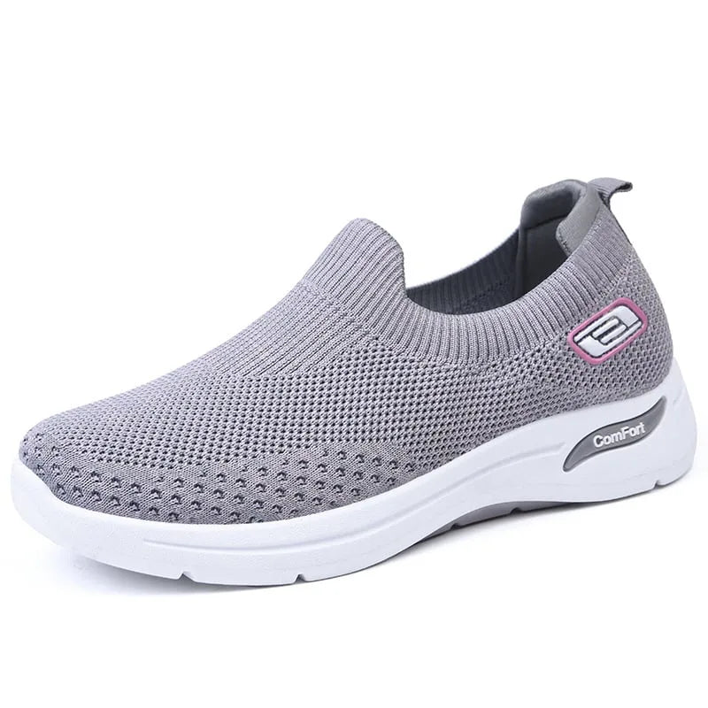 Side view of grey knit slip-on sneaker with pink accent logo tab and thick white midsole