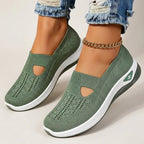 Sage green knitted slip-on sneakers with cut-out detail, white chunky sole and gold-tone side logo, worn on bare feet
