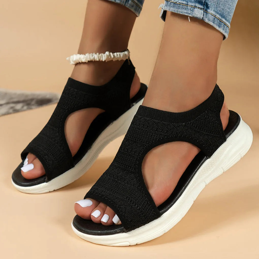 Black knit sport sandals with cut-out side panels and open toe, shown on model with white chunky sole