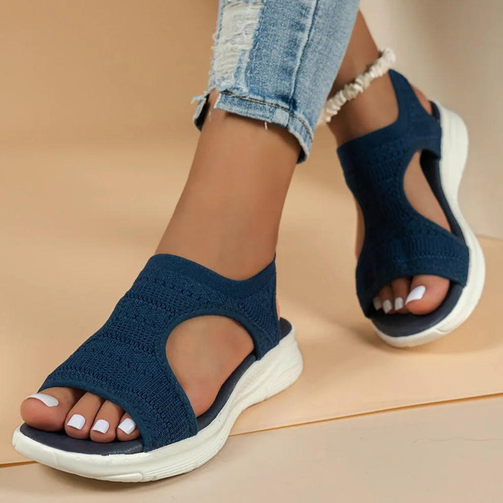 Dark blue knit sport sandals viewed in motion, showing open heel strap and thick white midsole