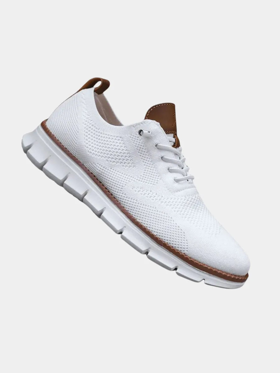 Angled top view of a white knit sneaker with tan leather heel pull-tab and chunky white ribbed sole