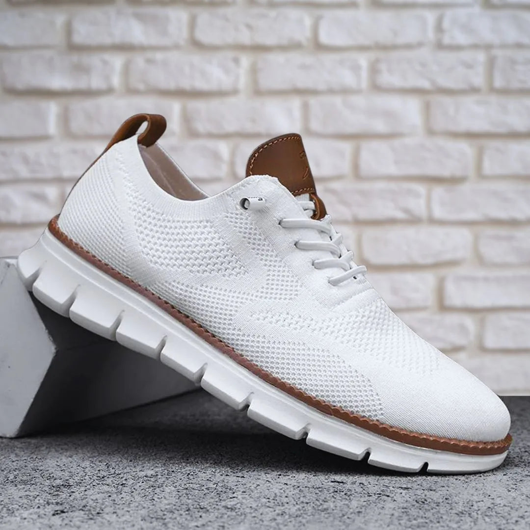 White knit lace-up sneaker against a white brick backdrop, highlighting the segmented white outsole