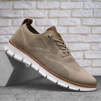 Beige knit lace-up sneaker resting on a concrete block, showing tan heel tab and white sole