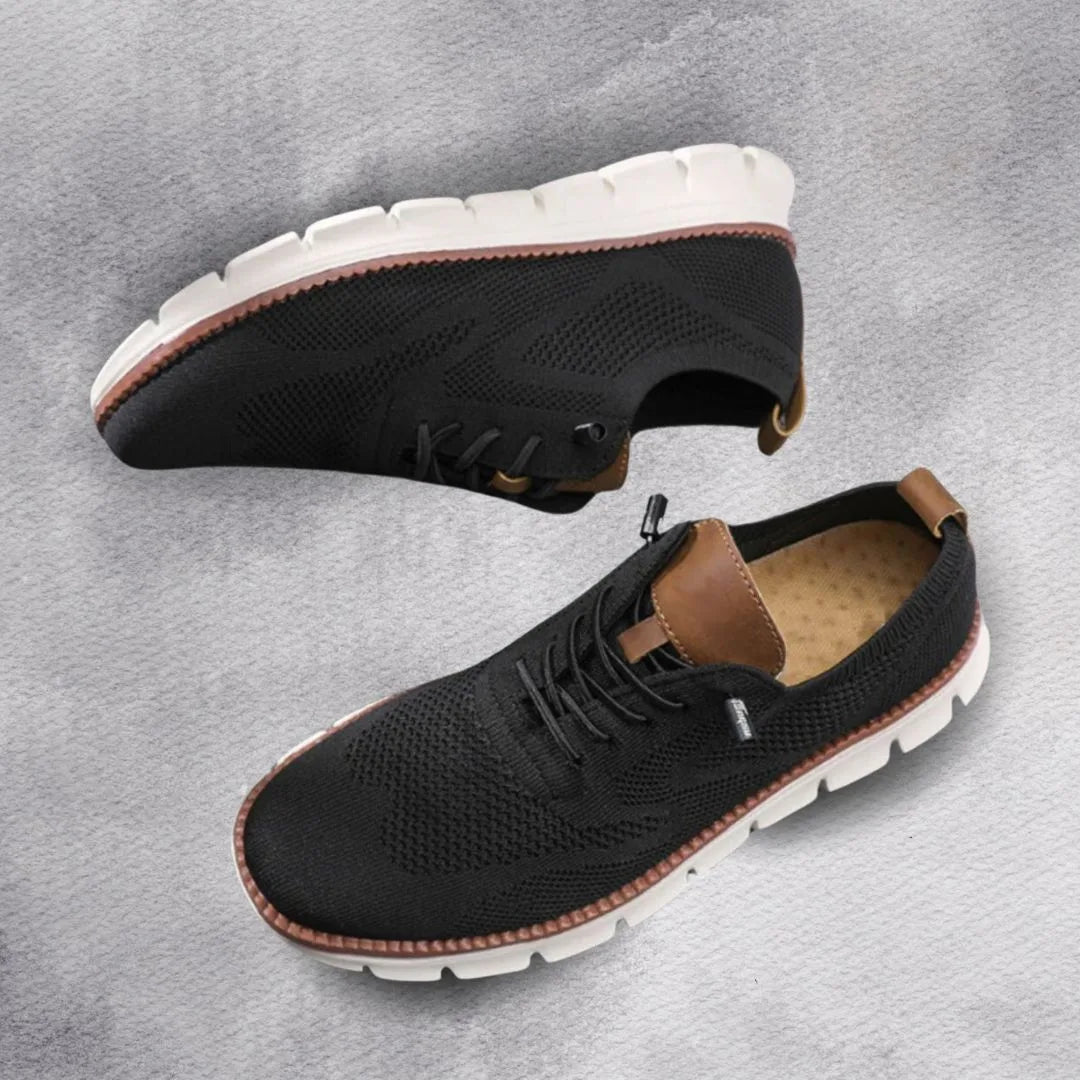 Pair of black knit sneakers on a grey marble surface showing tan leather heel trim and white sole