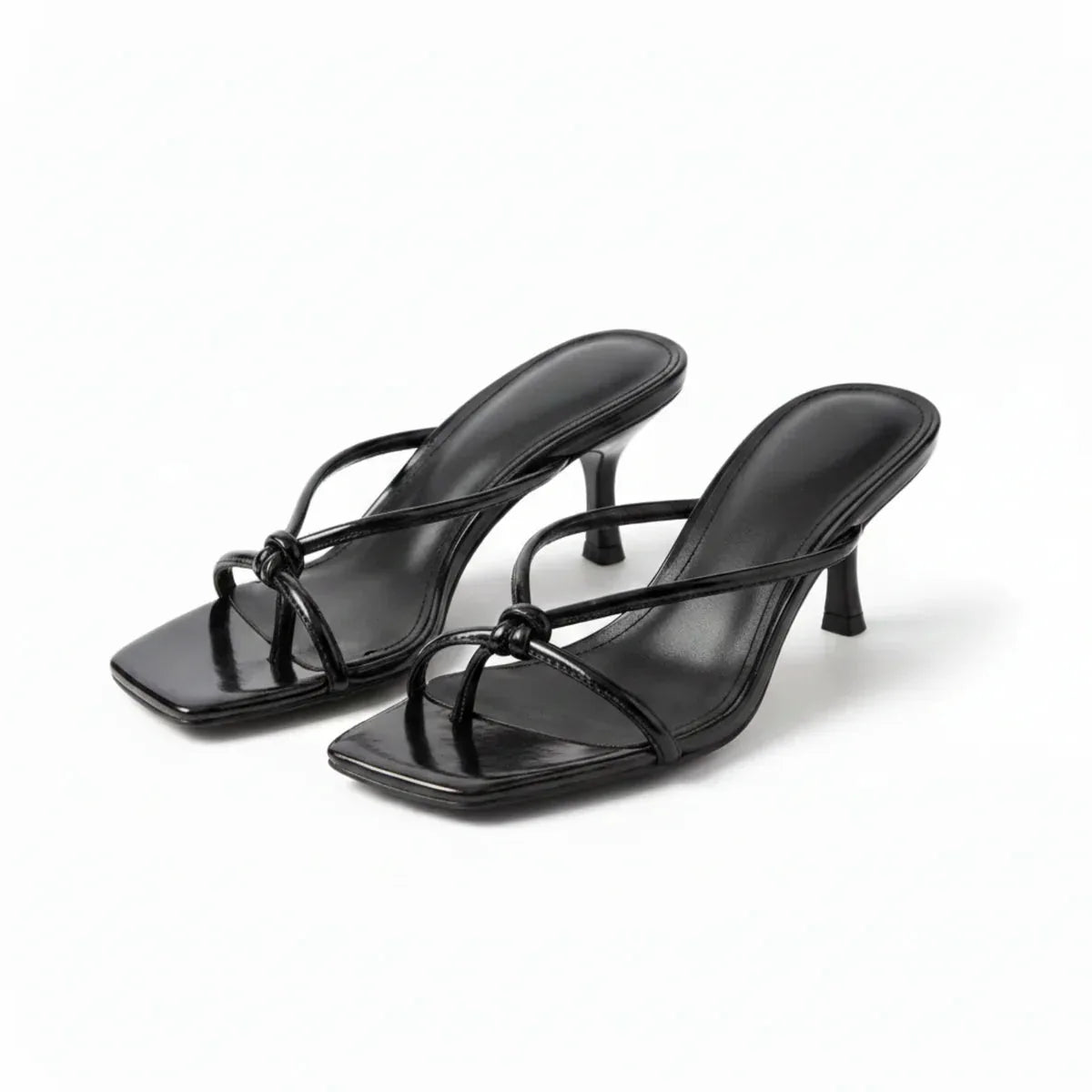 Pair of black strappy heeled sandals with knot detail, angled view on plain background
