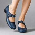Navy blue leather Mary Jane flats with teardrop cut-out detail and silver buckle strap, shown on crossed ankles