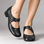 Black leather Mary Jane flats with teardrop cut-outs and silver buckle, shown from the front on crossed ankles