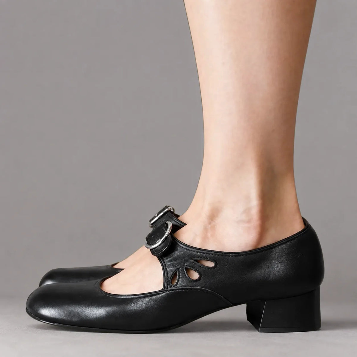 Side profile of black leather Mary Jane flats with low block heel, buckle strap and cut-out detailing