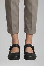 Close-up front view of black leather Mary Jane flats with buckle strap and cuffed trousers