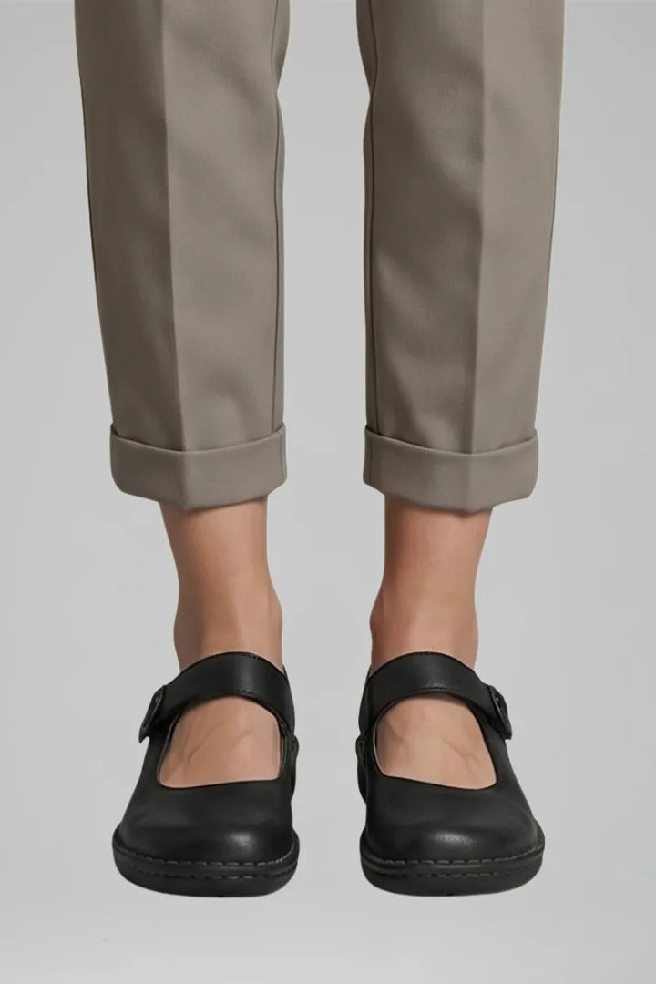 Close-up front view of black leather Mary Jane flats with buckle strap and cuffed trousers