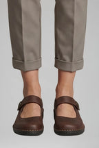 Close-up front view of brown leather Mary Jane flats with button strap closure and cuffed trousers