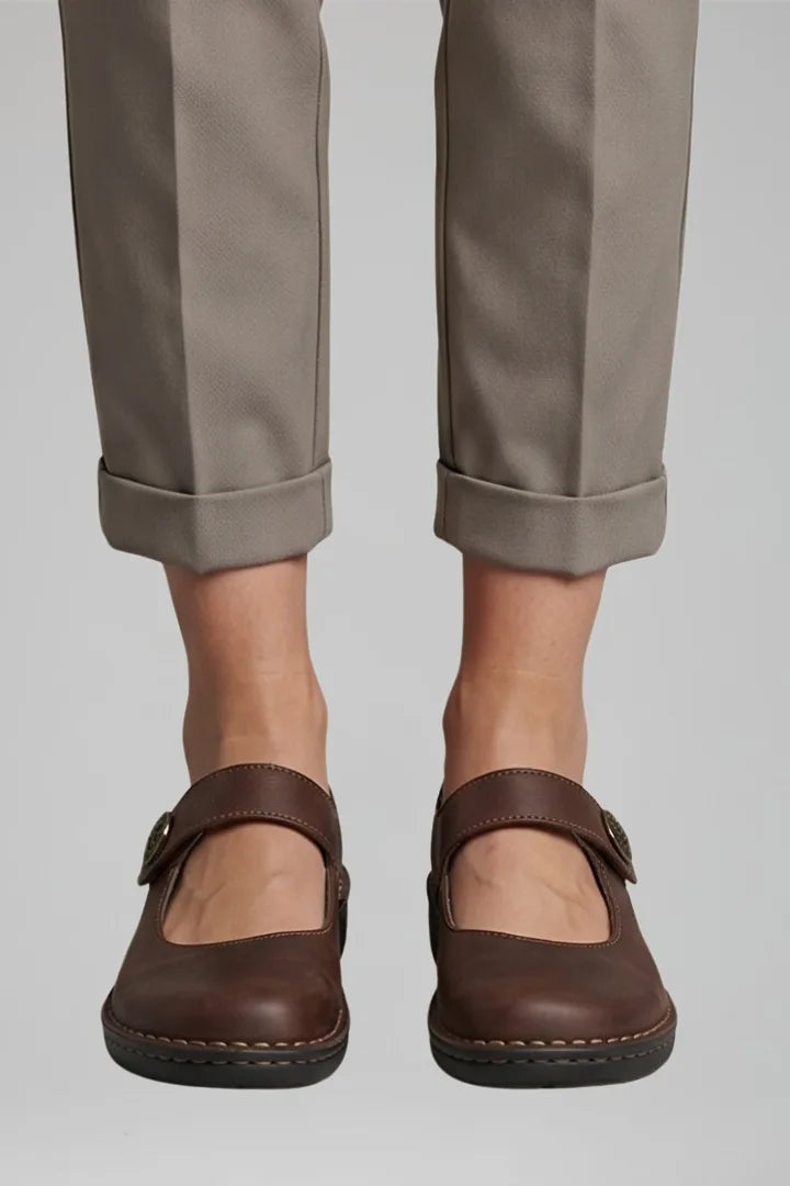Close-up front view of brown leather Mary Jane flats with button strap closure and cuffed trousers